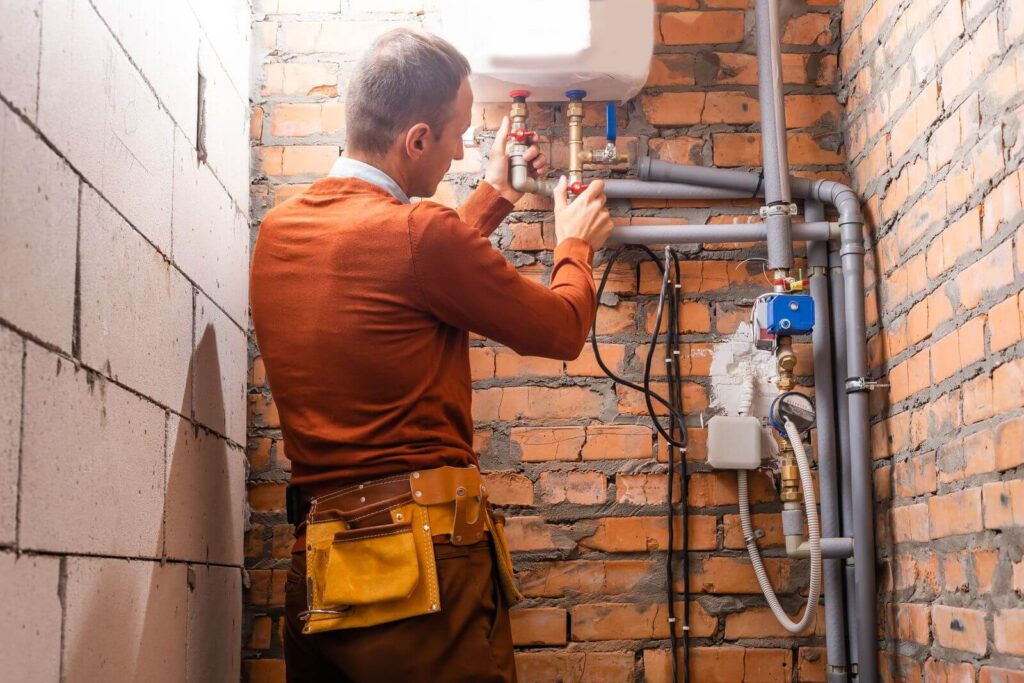 A plumber checking pipes in a into a water heater pump