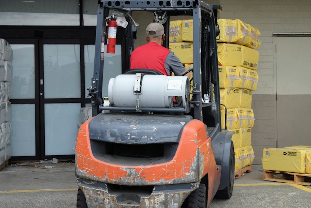 An orange forklift from the back, carrying yellow bags