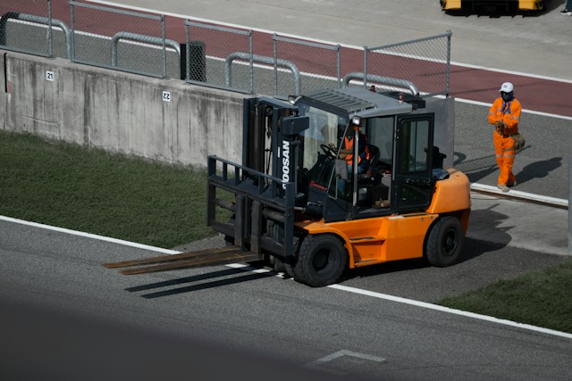 A large forklift exiting an industrial area, turning onto a road.