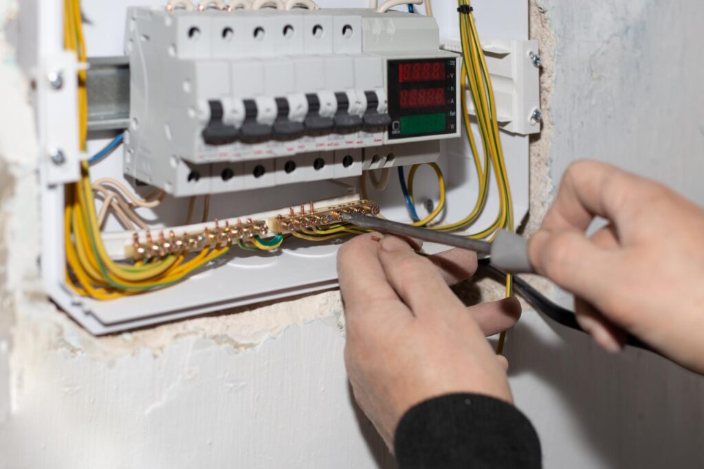 Close up of hands holding a screwdriver, working on an electrical switch boards.