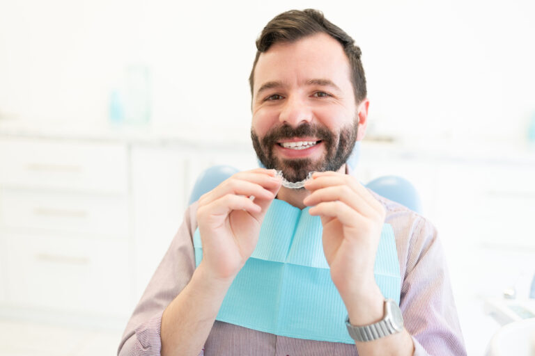 Smiling man holding a teeth aligner.