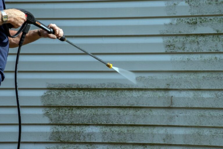 A person using a pressure washer to clean exterior house siding, removing mould and mildew for a fresh, well-maintained look.