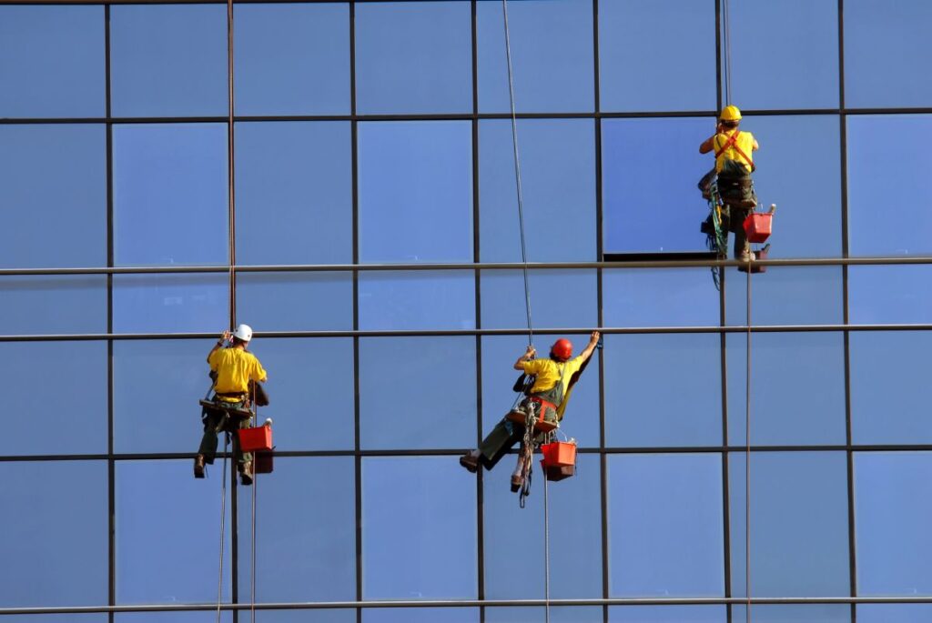 Rope access height workers cleaning and maintaining a tall glass façade on a high-rise building.